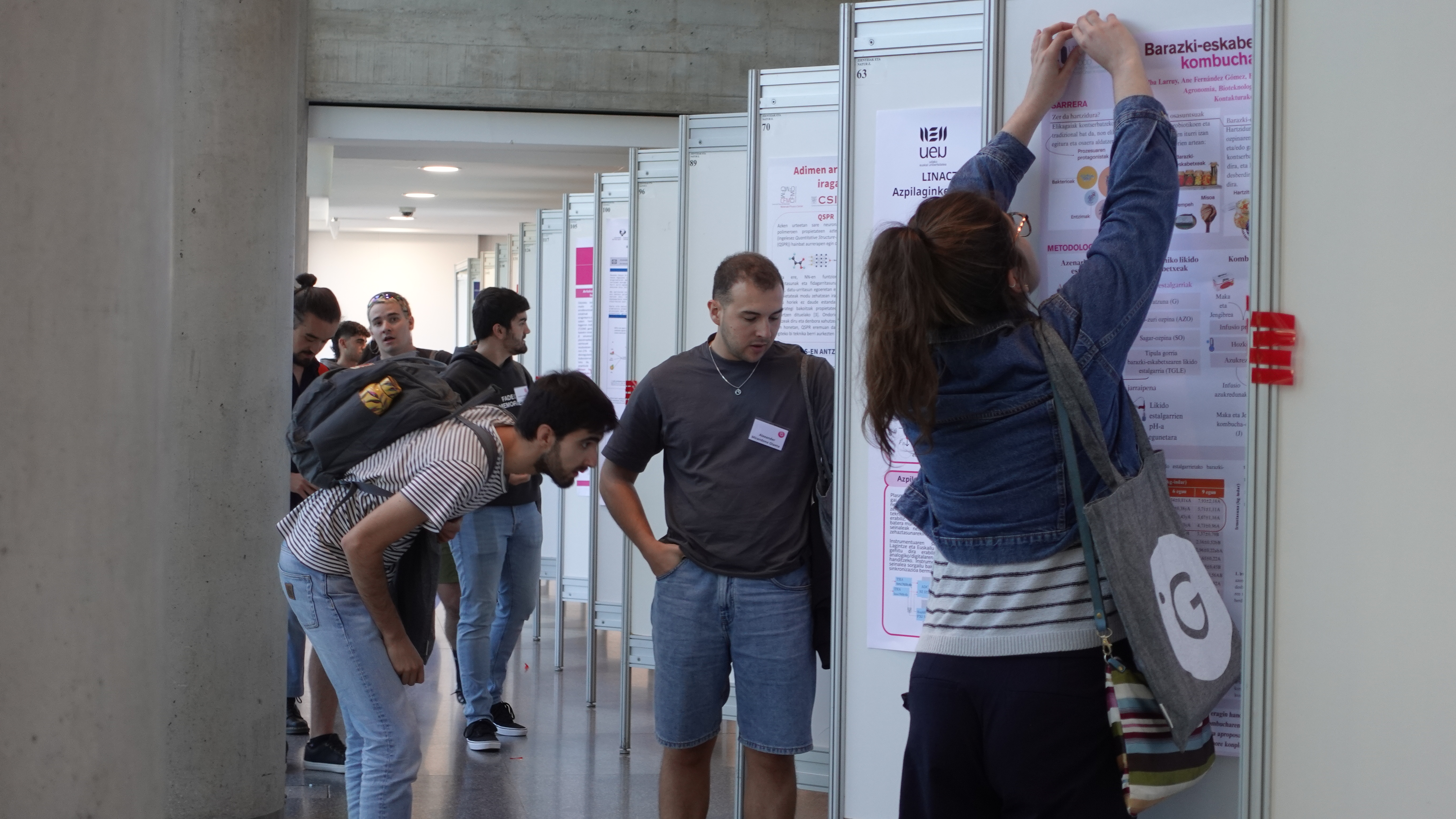 Ikergazte kongresuan posterrak jartzen ageri da ikertzaile bat. Eta beste hainbat ikertzaile jarrita dauden posterrei begira